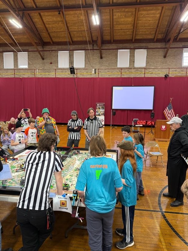 Teams and referees gathered around robot game tables in a gym